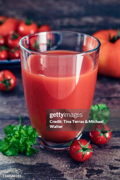 a glass of tomato juice in front of a dark wood background. - tomatensap stockfoto's en -beelden