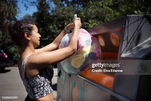 young woman putting old clothes into a bin at a recycling centre - mixed recycling bin stock pictures, royalty-free photos & images