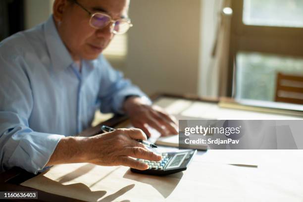 hombre mayor calculando las finanzas - calculadora fotografías e imágenes de stock