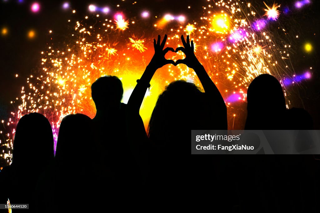 Rear view of young woman silhouette making heart shape symbol at firework celebration