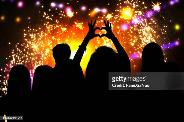 rear view of young woman silhouette making heart shape symbol at firework celebration - crowd hand heart stock pictures, royalty-free photos & images