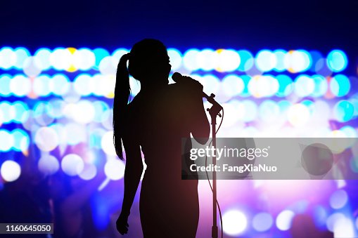 Silhouette der Frau mit Mikrofongesang auf der Konzertbühne vor Publikum Silhouette der Frau mit Mikrofongesang auf der Konzertbühne vor Publikum