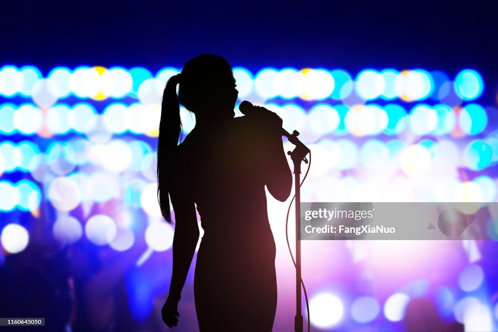 Silueta de mujer con micrófono cantando en el escenario de conciertos frente a la multitud