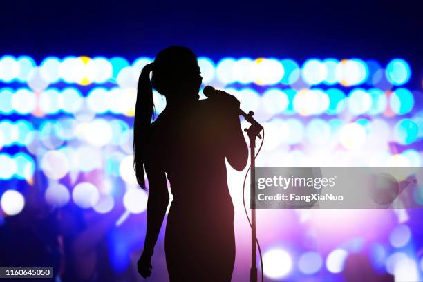 silueta de mujer con micrófono cantando en el escenario de conciertos frente a la multitud - club singer fotografías e imágenes de stock