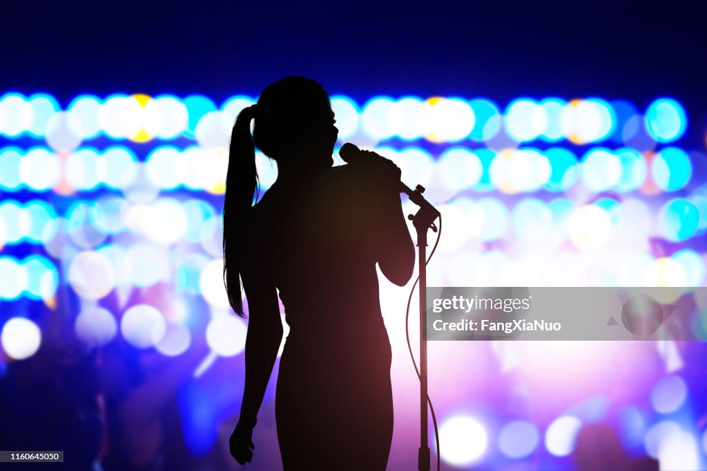 Silhouette de femme avec le microphone chantant sur la scène de concert devant la foule