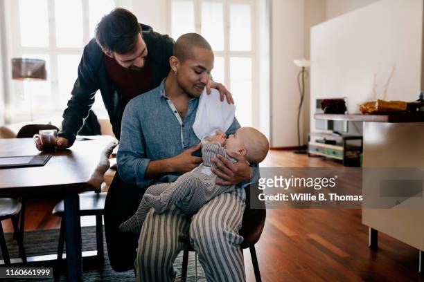 black gay father and partner feeding baby bottle - person gemischter abstammung stock-fotos und bilder