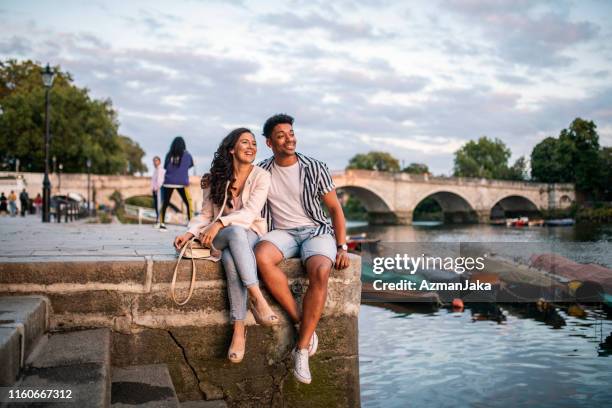 smiling couple sitting on embankment in richmond upon thames - richmond upon thames imagens e fotografias de stock