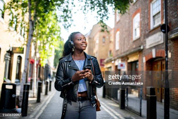 mature adult african woman listening to music while walking streets of london - hackney london stock pictures, royalty-free photos & images