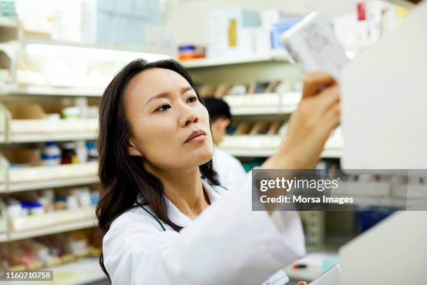 female pharmacist arranging drugs on shelf - pharmacist fotografías e imágenes de stock