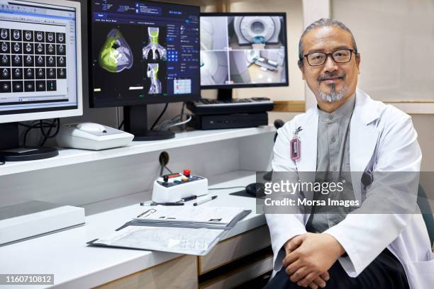 Confident mature doctor sitting by desk in office