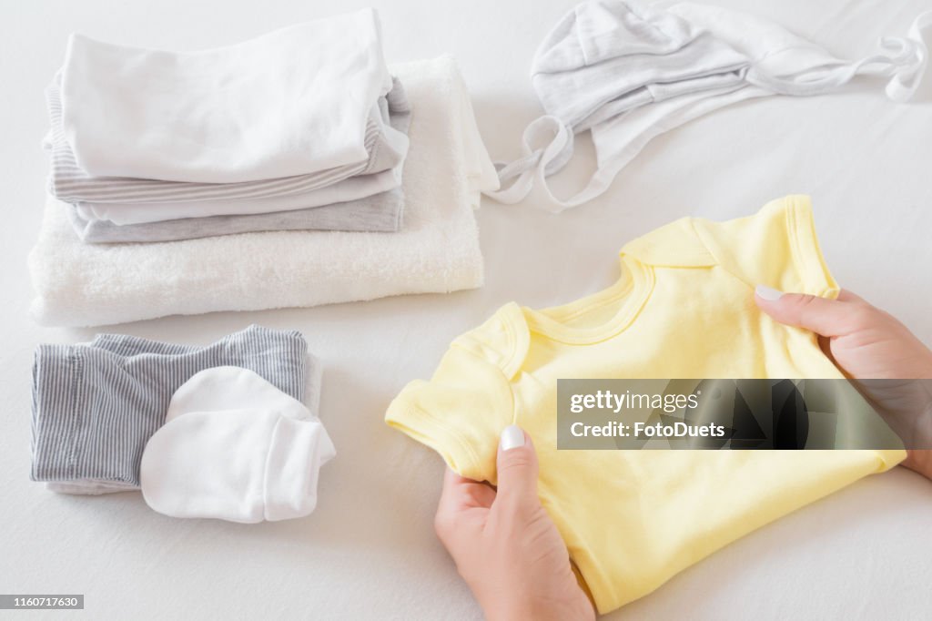 女人的手在白色的床單上整理新的嬰兒衣服。母親的日常職責。柔和的顏色。特寫。