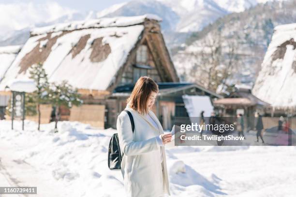 mooie aziatische vrouw toerist houdt de kaart tour met witte sneeuw winter op shirakawa-go village, japan - shirakawa go stockfoto's en -beelden