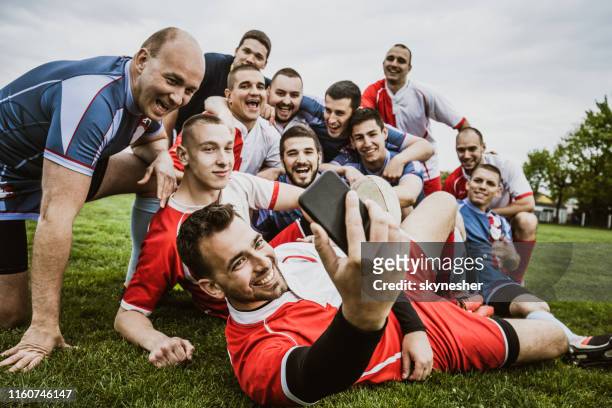 glückliche rugby-spieler, die ein selfie mit handy auf einem spielfeld machen. - rugby liga stock-fotos und bilder