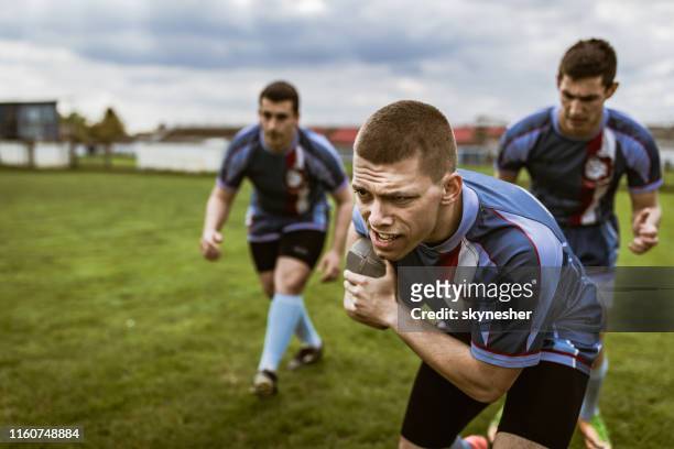 entschlossene rugbyspieler, die mit ball auf einem spielfeld laufen. - rugby liga stock-fotos und bilder