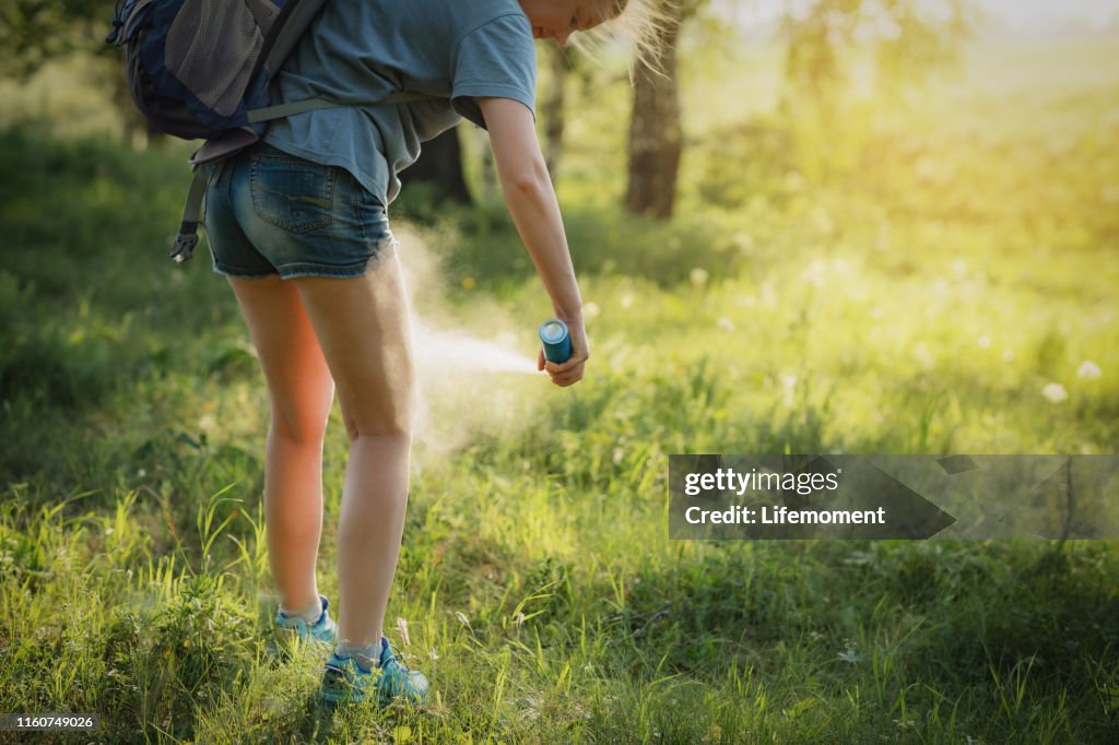 Hiker applying mosquito repellent on the leg skin in the forest.