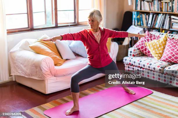 senior woman doing yoga in the living room of her home - senior adult yoga stock pictures, royalty-free photos & images