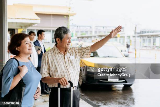 senior-paar hailing taxi im regen vor flughafen - airport rain stock-fotos und bilder