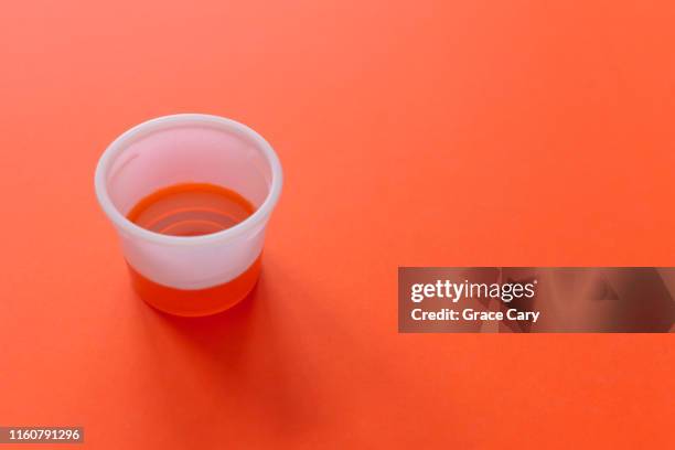 cup of cough syrup against a bright orange background - medicina para los resfriados fotografías e imágenes de stock