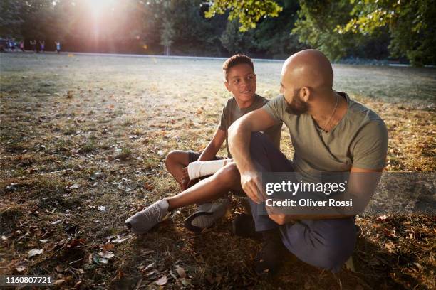 father and son sitting on meadow in a park - ray oliver stock pictures, royalty-free photos & images
