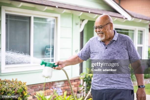 senior black man watering outdoor plants - lawn fertilizer stock pictures, royalty-free photos & images