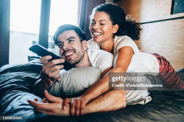 beautiful couple watching tv in the bedroom - lazy husband stock pictures, royalty-free photos & images