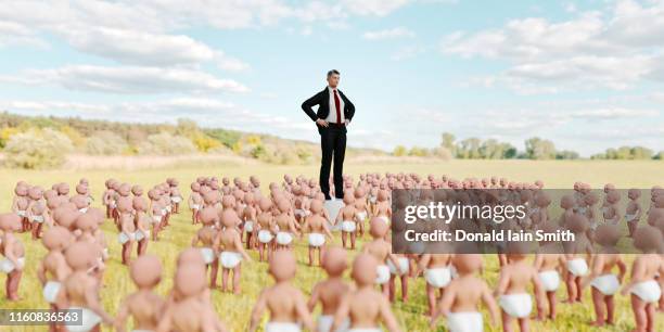 man standing on plinth surrounded by multiple babies in field - capitalism stock pictures, royalty-free photos & images