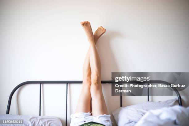 woman with legs raised wearing white shorts lying on bed - voeten omhoog stockfoto's en -beelden