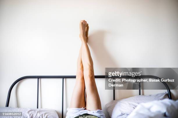 woman with legs raised wearing white shorts lying on bed - feet in bed stock-fotos und bilder
