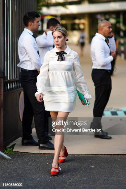 Guest wears a white dress with a black bow collar, red Miu Miu Mary Jane pumps, outside Miu Miu Club 2020, on June 29, 2019 in Paris, France.