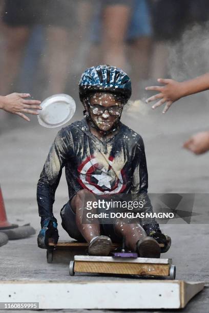 Boy competes in a downhill-kart racing known as "Mundialito de Rolima do Abacate" as flour is thrown against him as part of obstacles from attendants...
