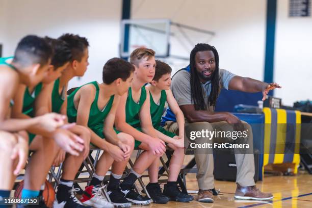 elementary boys basketball team sitting on the sideline bench with their coach - basketball sideline stock pictures, royalty-free photos & images