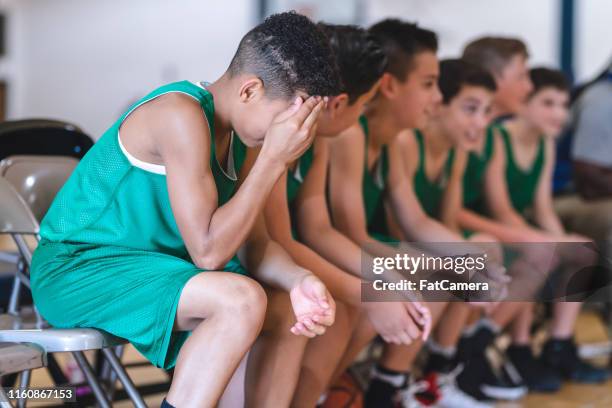 elementary boys basketball team sitting on the sideline bench with their coach - basketball sideline stock pictures, royalty-free photos & images