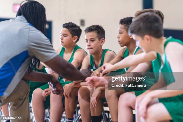 elementary boys basketball team sitting on the sideline bench with their coach - basketball sideline stock pictures, royalty-free photos & images