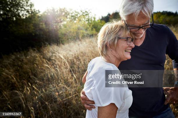 happy mature couple embracing in a field - brille paar stock-fotos und bilder