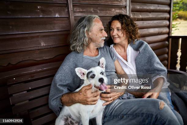 mature couple with dog sitting on porch of a log cabin - linda oliver fotografías e imágenes de stock