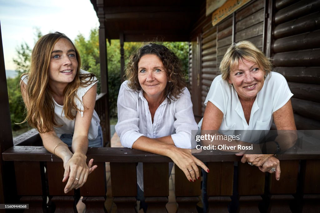 Portrait of three women leaning on balcony of a log cabin