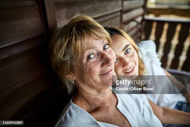 portrait of mother and adult daughter sitting on porch of a log cabin - mid adult women photos et images de collection