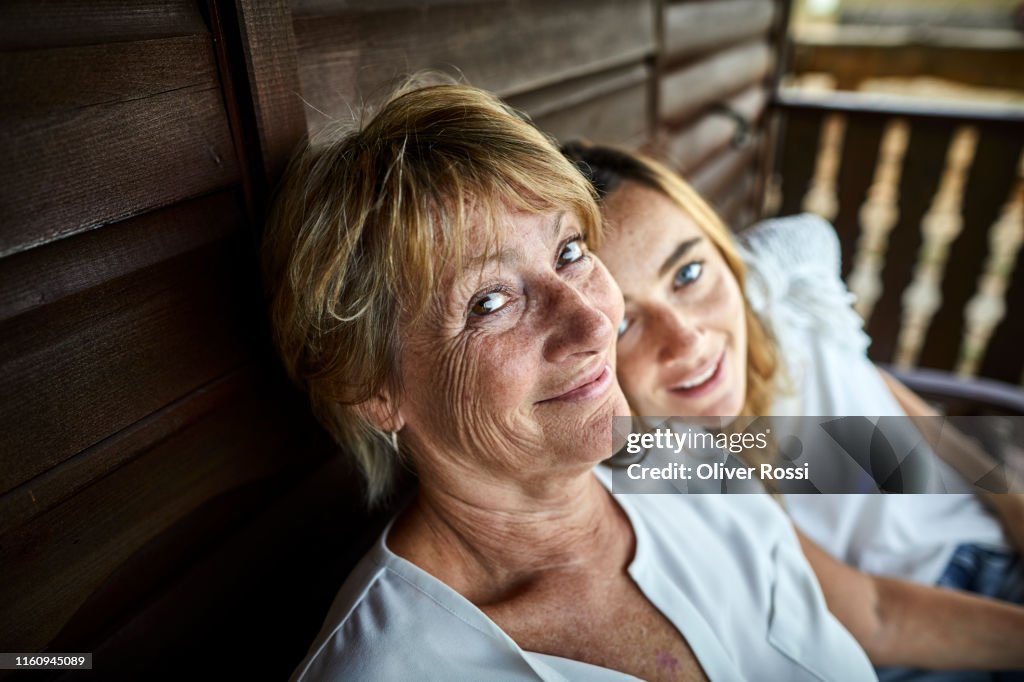 Portrait of mother and adult daughter sitting on porch of a log cabin
