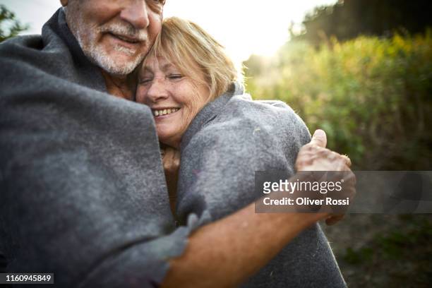 mature couple wrapped in a blanket cuddling in the countryside - senior woman portrait stock-fotos und bilder