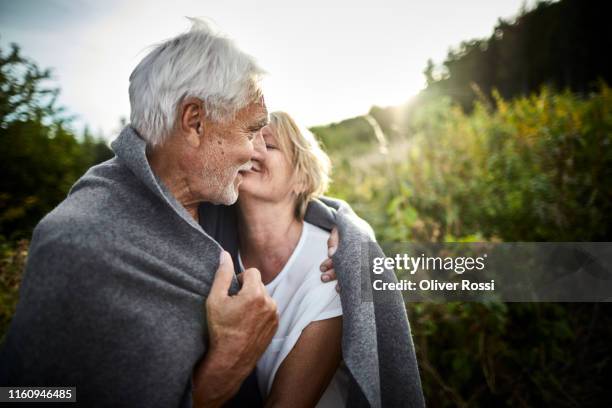 mature couple wrapped in a blanket cuddling in the countryside - reifes paar stock-fotos und bilder