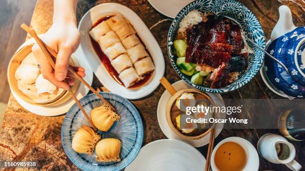 flat lay chinese dim sum time, various traditional dim sum freshly served on table and human hands picking up with chopsticks - dimsum stock pictures, royalty-free photos & images