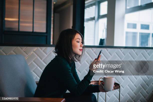 smiling, confident, modern businesswoman taking coffee break and checking social media at mobile phone in office - cool attitude stock pictures, royalty-free photos & images