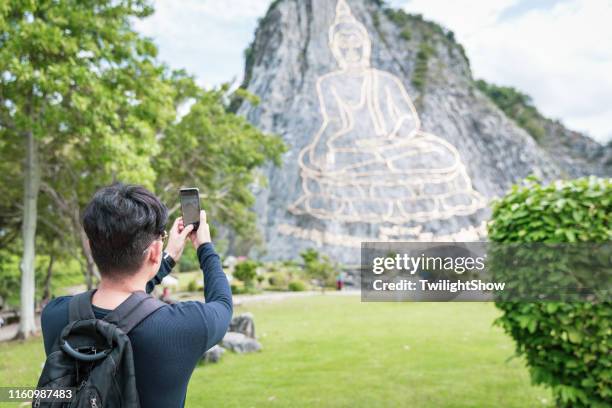 young asian man travelling alone taking photo with smartphone at khao chi chan - pattaya stock pictures, royalty-free photos & images