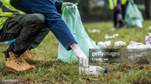 picking up a plastic bottle during park clean-up - limpeza ambiental imagens e fotografias de stock