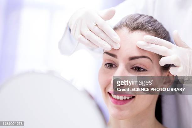 doctor examining young woman's forehead - dermatologia fotografías e imágenes de stock