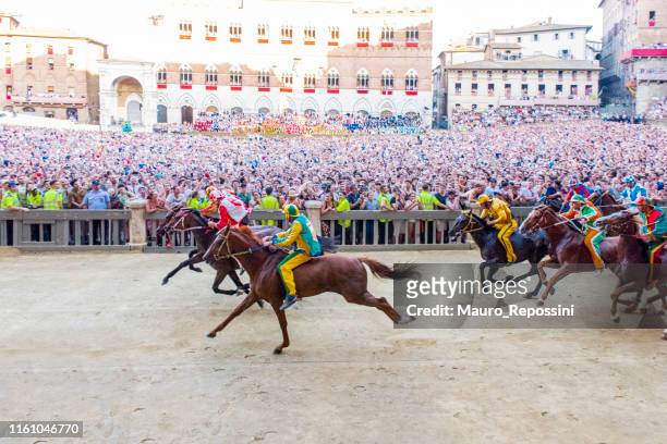 horses competing during the first lap of the 2019 palio di siena in the "piazza di campo" at the city of siena in tuscany, italy. - senna stock pictures, royalty-free photos & images