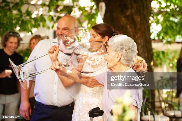 bruid en haar moeder in de wet het drinken van wijn uit grote wineglass bij wedding celebration - summer comedies party stockfoto's en -beelden