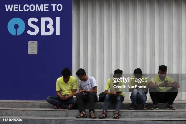 People use mobile phone as they sit outside State Bank of India branch in Mumbai, India on 11 August 2019. SBI has a network of more than 43,000 ATM...