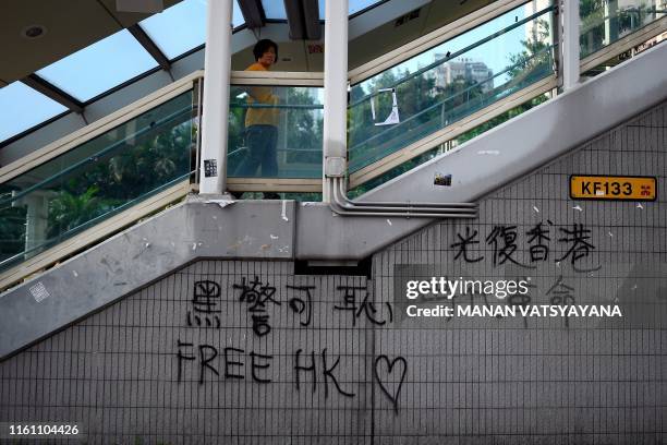 This picture taken on August 9, 2019 shows a woman walking on a pedestrian bridge adorned with "Free HK" graffiti in the Wong Tai Sin district of...