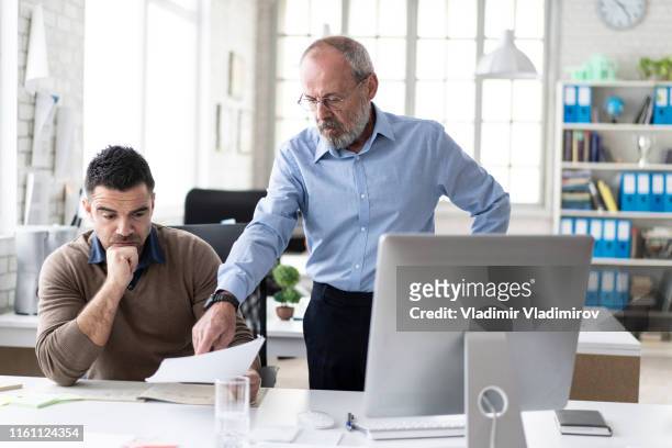 senior manager explaining to coworker something on computer - repreensão imagens e fotografias de stock